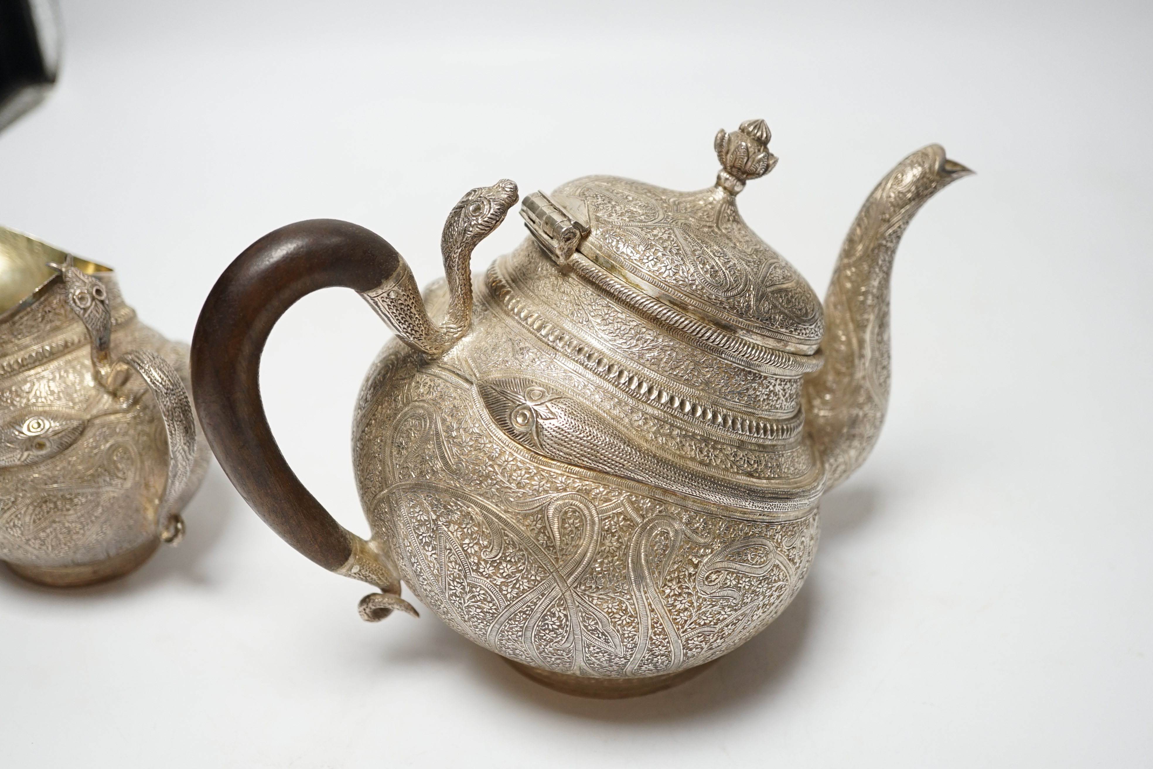 A 20th century Indian three piece embossed white metal tea set, with boteh and cobra decoration, gross weight 38.6oz.